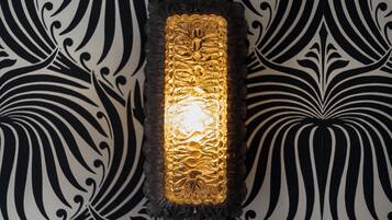 A wall-mounted light fixture with a textured, gold-colored design, set against a black and white patterned wallpaper.