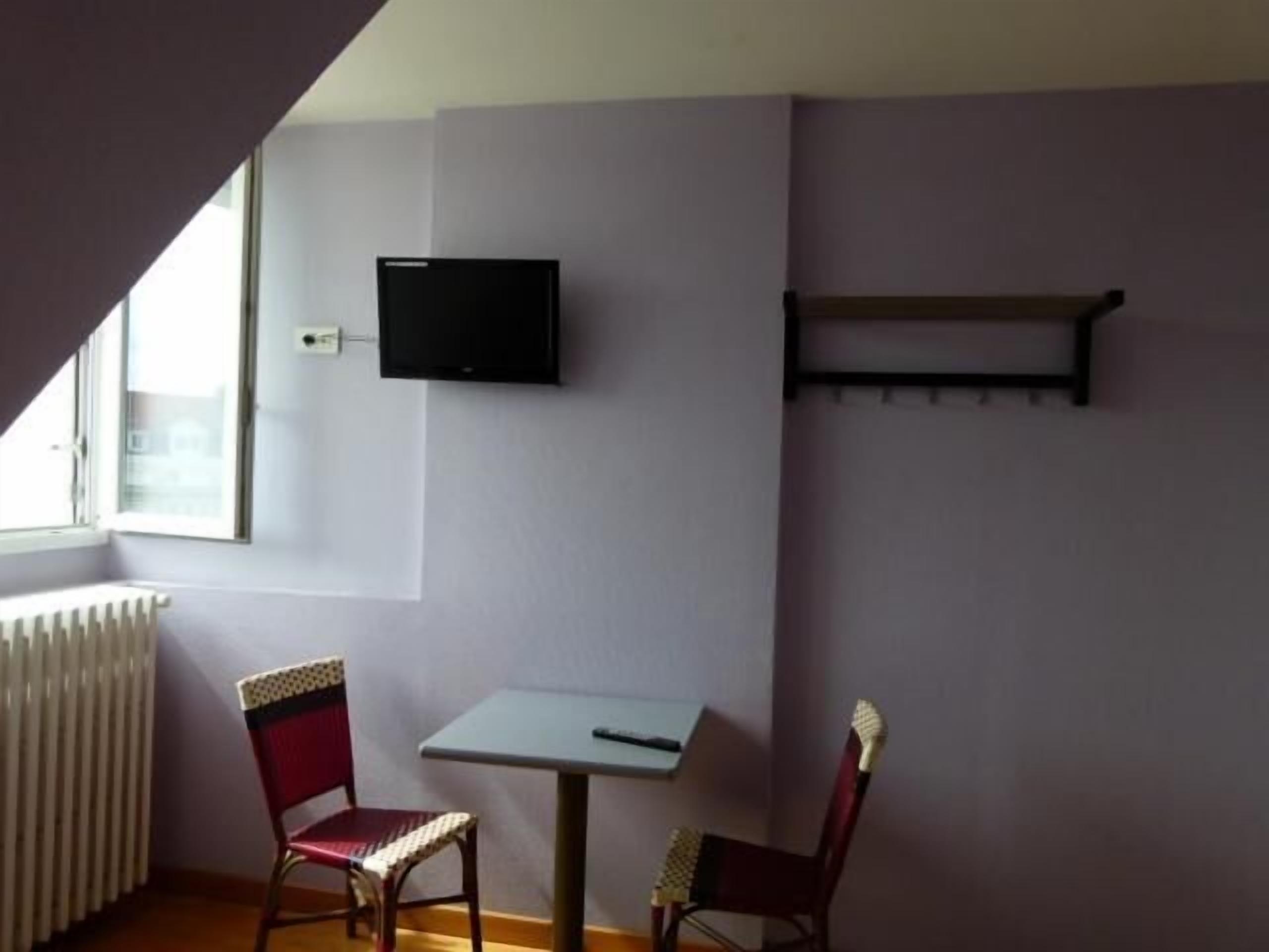 A small room with a white radiator, a table, two chairs, a TV mounted on the wall, and a window with a view.