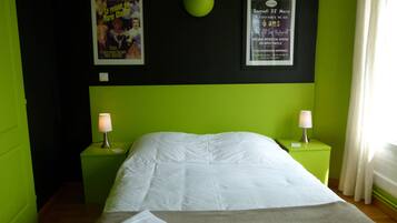 A room with a bed, green walls, two nightstands with lamps, and posters on the wall.