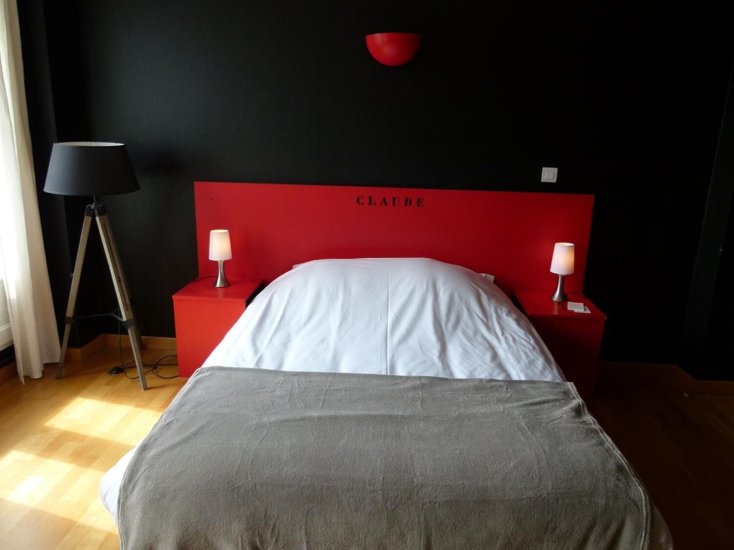 A hotel room with a red headboard, a bed with white bedding, two bedside lamps, and a red bowl on the wall.