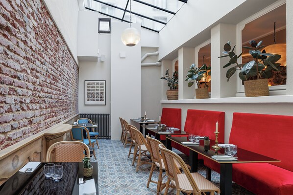 Un restaurant avec un mur en briques, des chaises en bois, un canapé rouge et des plantes en pot.