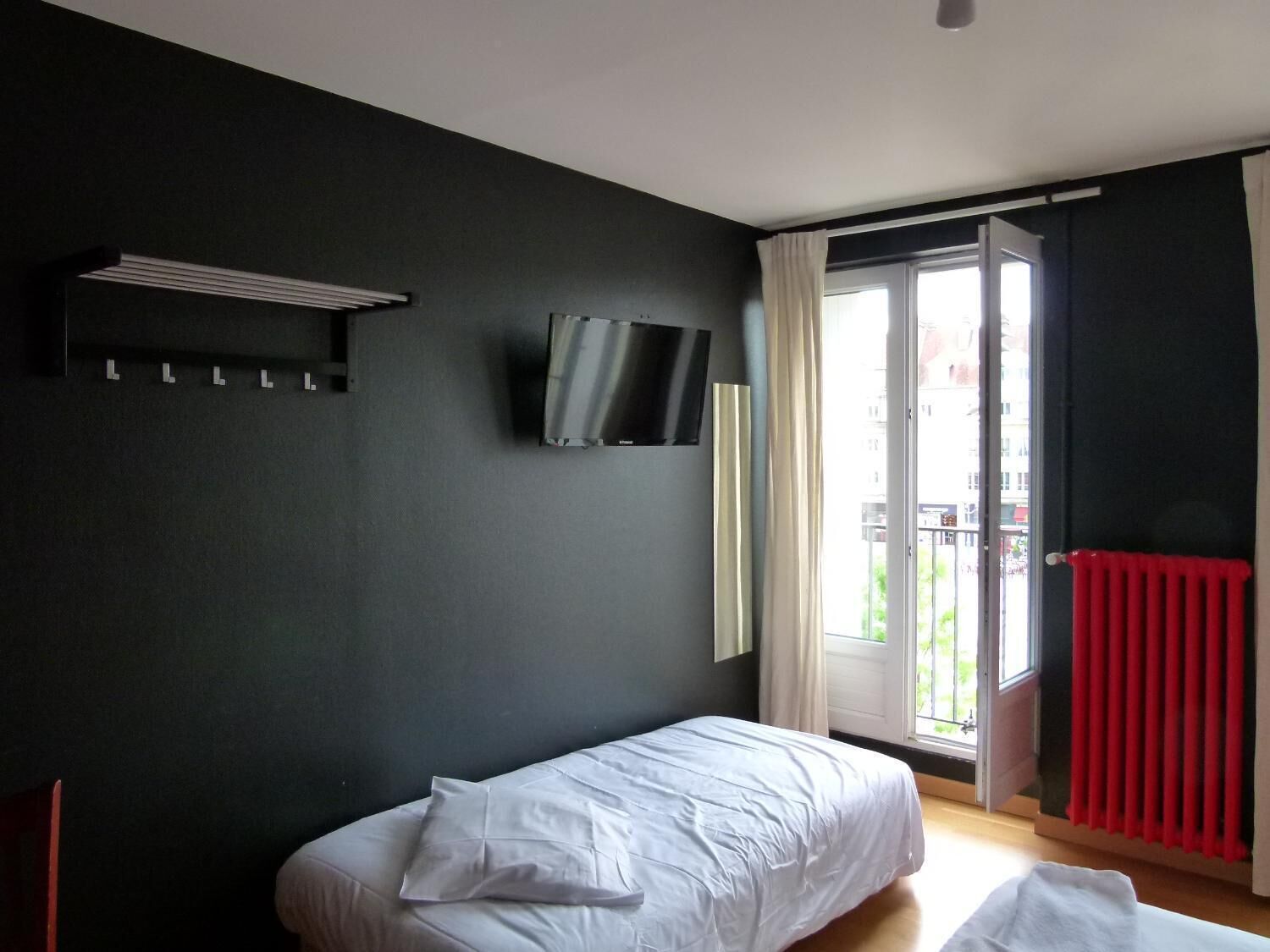 Un dormitorio con cama, televisor montado en la pared, ventana con cortinas y radiador.
