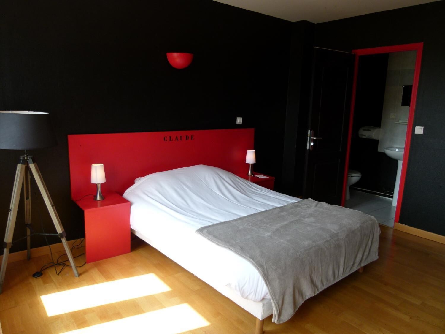Une chambre à coucher moderne avec une tête de lit rouge, un lit blanc, une table de chevet avec une lampe et une lampe sur pied.