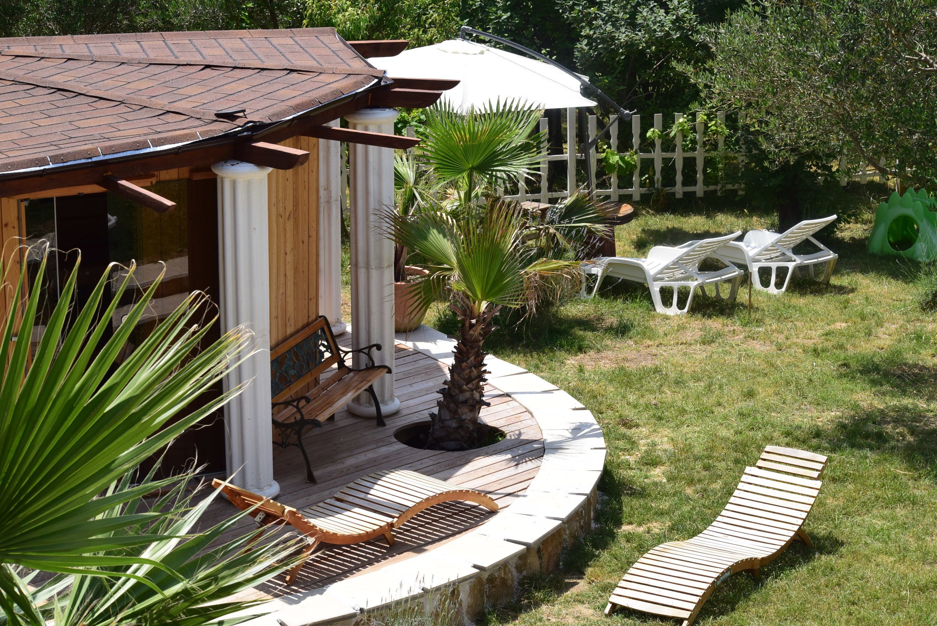 A wooden deck with a palm tree, a bench, and two lounge chairs.