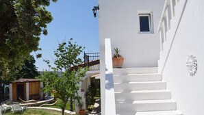 A white building with a staircase leading to a balcony. There are potted plants on the ground and a small wooden structure in the background. - Villa Agata Rab - Apartments (Rab)