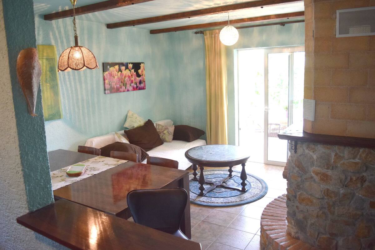 A living room with a dining area, a stone fireplace, a sofa, and a painting on the wall.