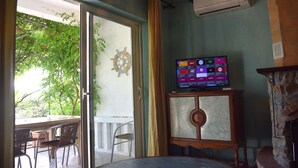 A room with a television on a wooden stand, a glass door leading to an outdoor area with chairs, and a wall-mounted air conditioner. - Villa Agata Rab - Apartments (Rab)