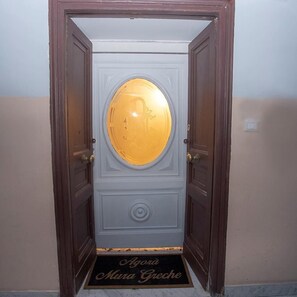 A door with a circular glass panel, a doormat with text, and a light switch on the wall. - B&B Agorà Mura Greche (Naples)