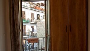 Un dormitorio con cama, armario de madera y balcón con vistas a edificios.