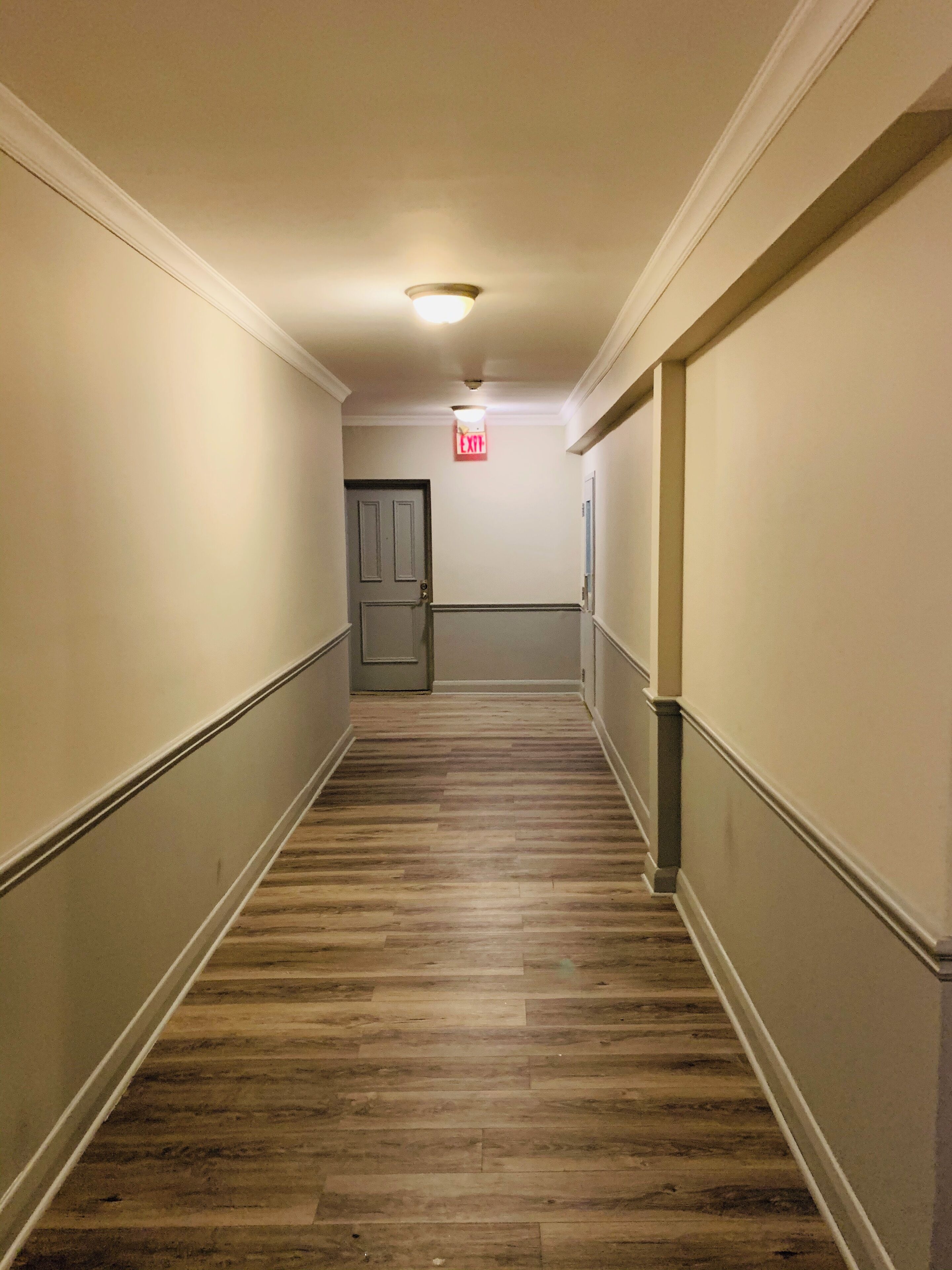 Un couloir avec un plancher en bois, des murs blancs et une porte au fond.