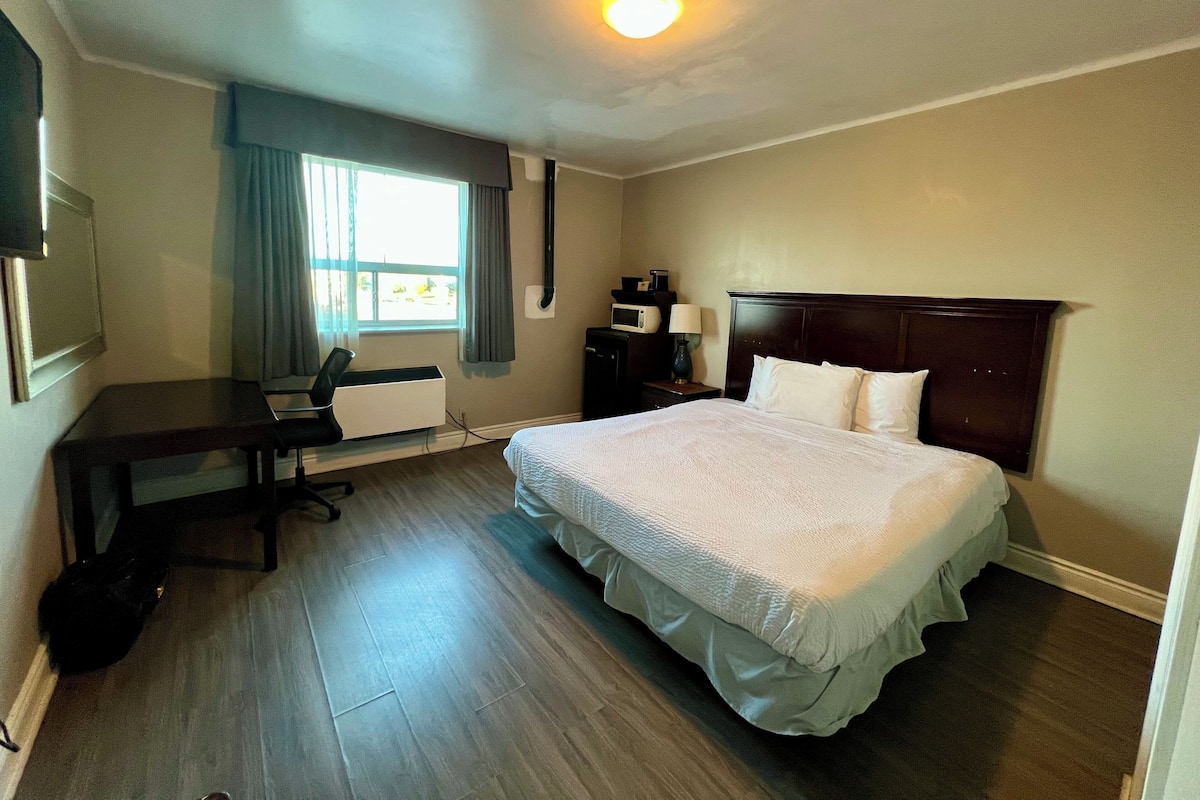 A hotel room with a bed, desk, chair, and a window with curtains.