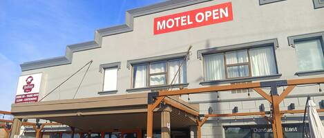 Un motel con un letrero que indica que está abierto, un comedor con mesas al aire libre y un letrero de 'prohibido estacionar'.