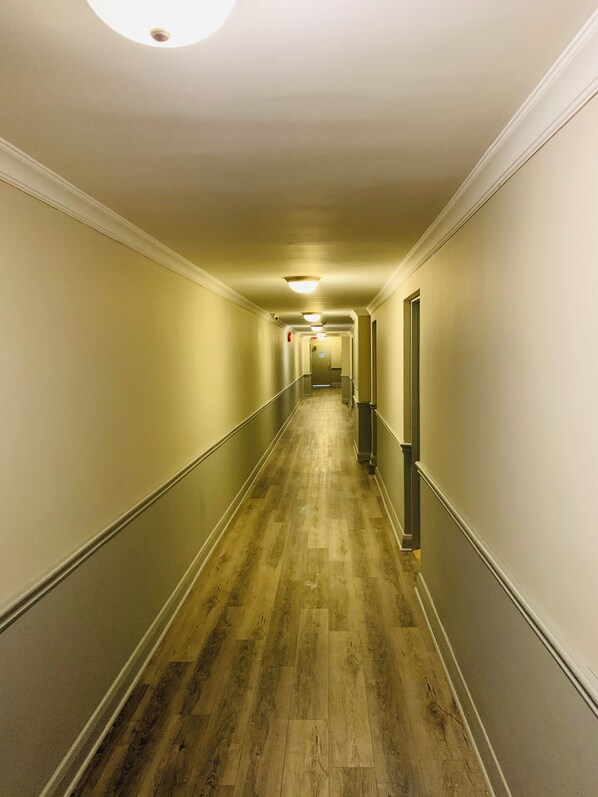 A long, narrow hallway with a wooden floor, white walls, and a metal railing on one side. - London Residency Inn (London)