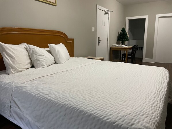 A neatly made bed with white bedding, a wooden headboard, and a small table with a Christmas tree. - London Residency Inn (London)