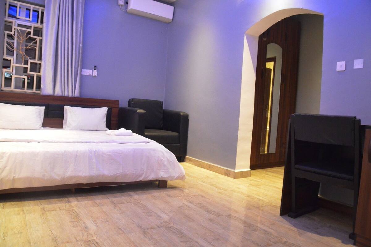 Habitación de hotel con cama, una silla, televisor y piso de madera.