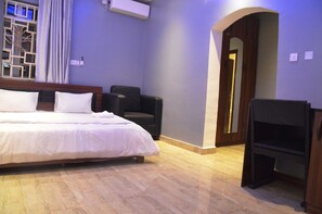 Habitación de hotel con cama, una silla, televisor y piso de madera.