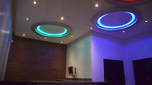 A modern interior with circular ceiling lights in blue and red, a wooden wall, and a small TV on a stand. - House X (Abuja)