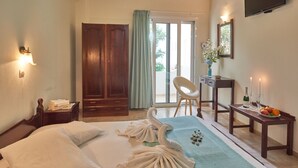 A hotel room with a bed, a desk, a chair, a TV, and a balcony with a view. - Corali Studios (Agios Vasileios)