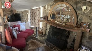 Una habitación acogedora con pared de piedra, chimenea, sofá rojo y televisor.