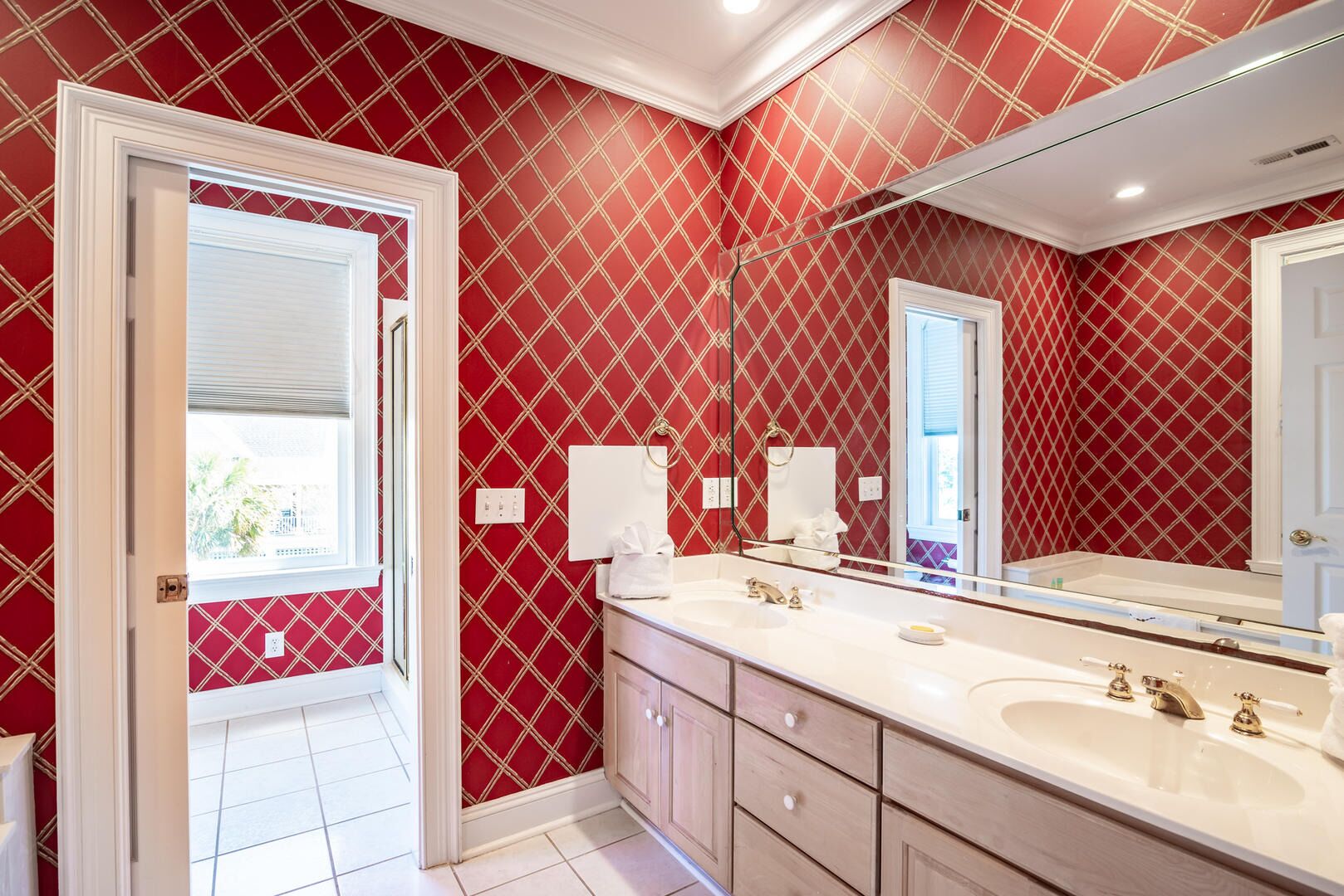 A bathroom with a red patterned wall, a white vanity, and a large mirror.