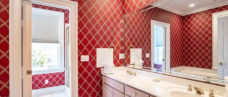 A bathroom with a red patterned wall, a white vanity, and a large mirror.