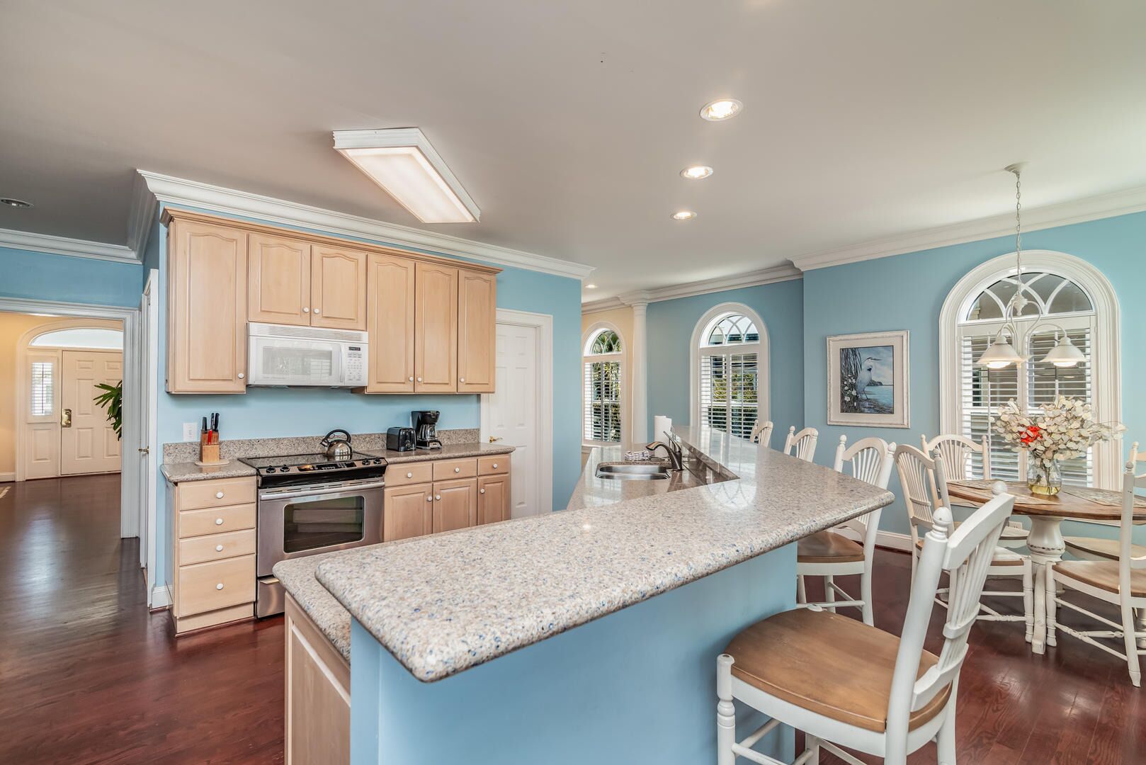 A spacious kitchen with a central island, wooden cabinets, and a dining area with white chairs and a table.