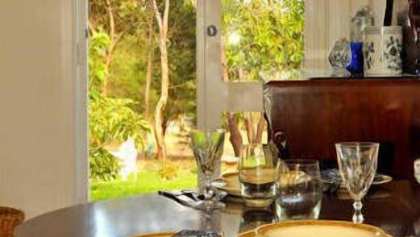 Een eetruimte met een tafel gedekt voor vier personen, een deur naar een tuin en een uitzicht op bomen en groen.
