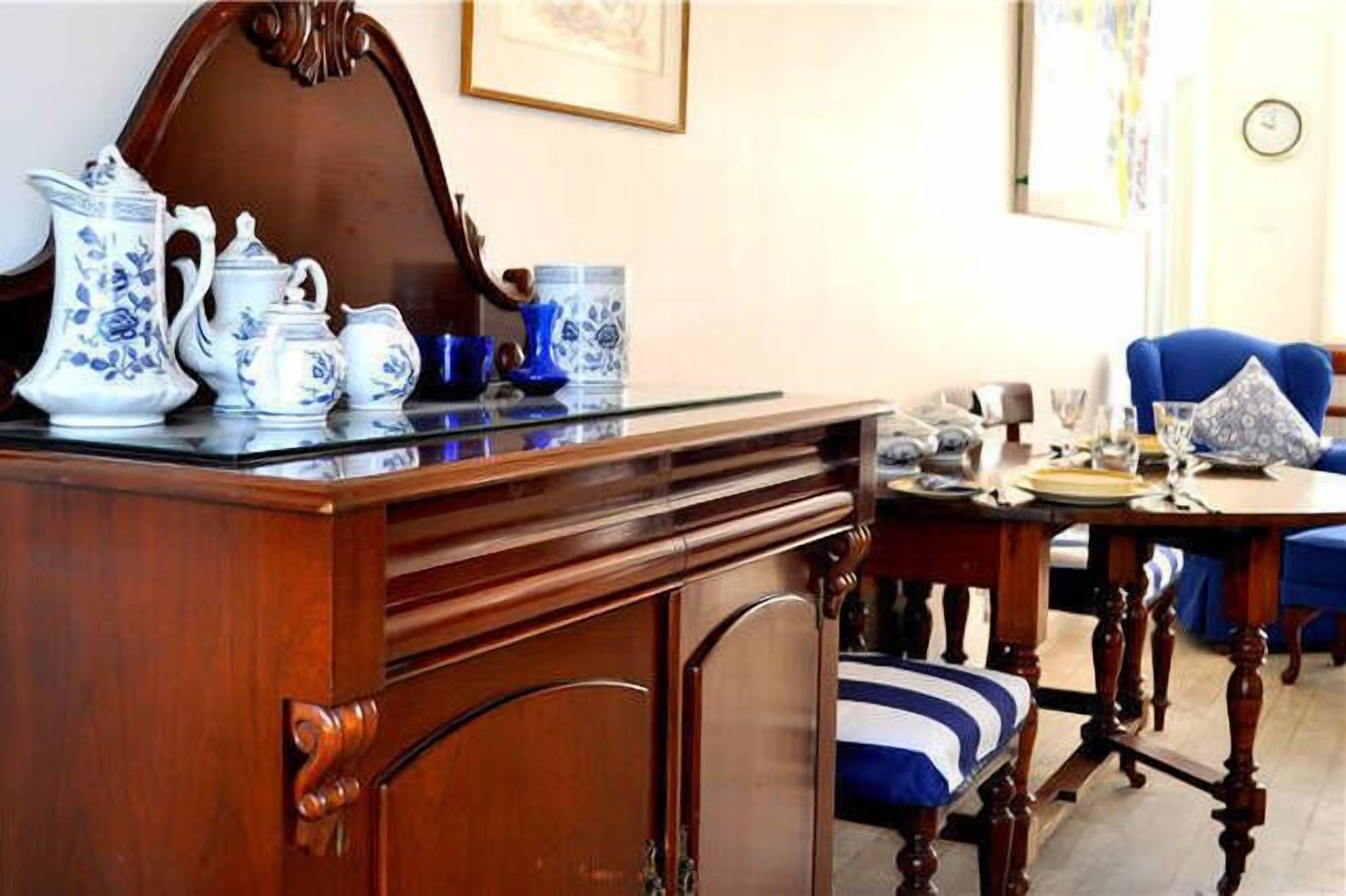 A dining area with a wooden table set for four, a blue upholstered chair, and a wooden cabinet with a mirror.