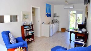 Een knus woongedeelte met een kitchenette, een eethoek en een zithoek met een blauwe bank en fauteuil.