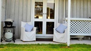 Een veranda met twee witte stoelen, een gasfles en een wit lattenhek.