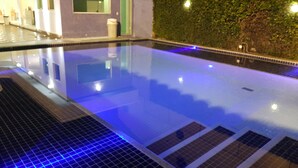 A swimming pool with a tiled deck and a green wall in the background. - House in a gated community in Barra da Tijuca  (RIO DE JANEIRO)