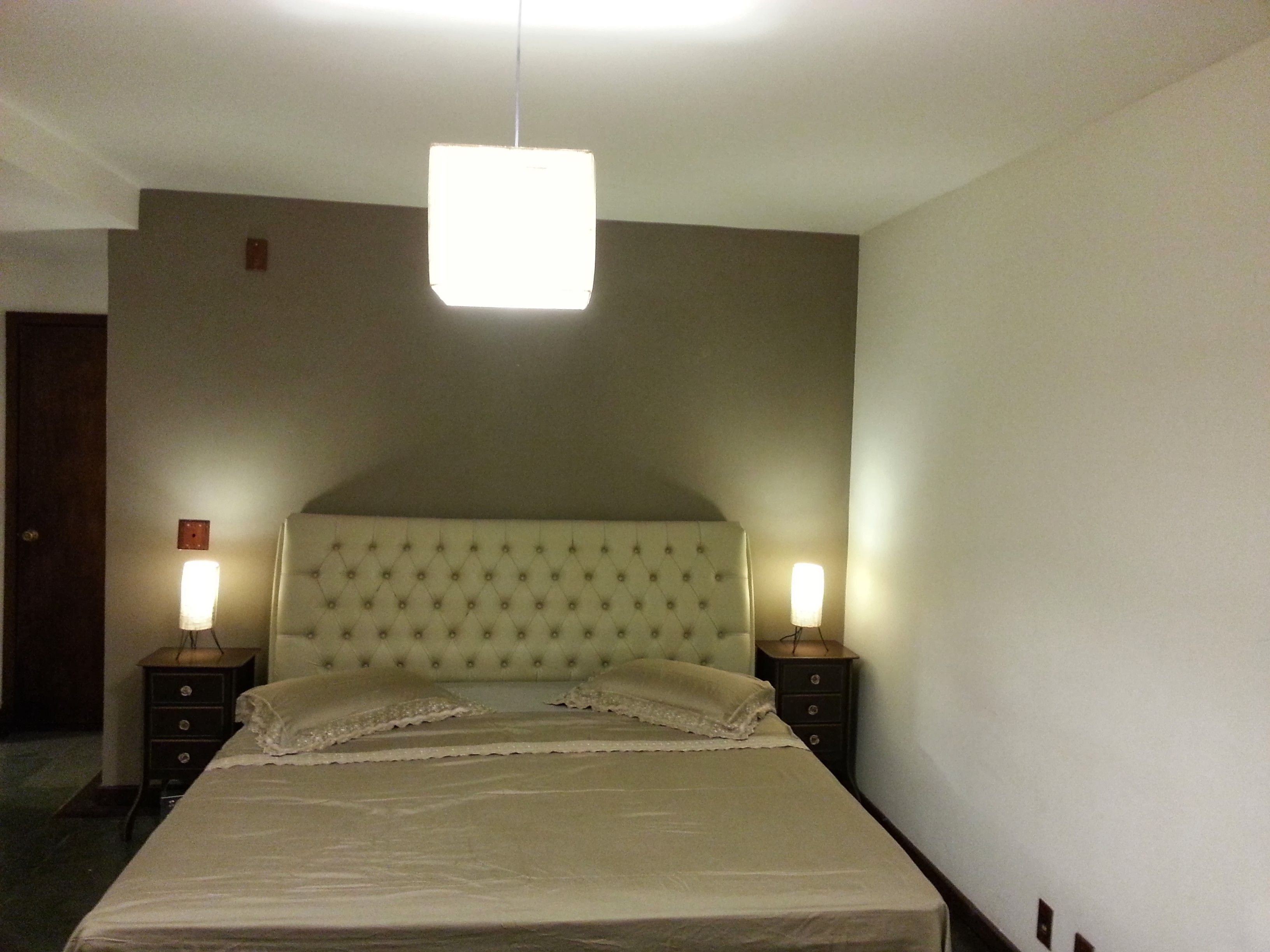 A neatly made bed with a tufted headboard, two bedside lamps, and a hanging light fixture.