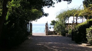 Un sentier de gravier mène à une plage, avec une porte en pierre et un banc.