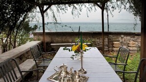 Une table dressée en plein air, avec vue sur la mer, des chaises en métal et une nappe blanche.