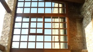 Une grande fenêtre à carreaux, encadrée dans un mur de pierres apparentes, avec une poutre en bois au-dessus.