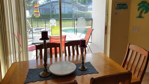 A dining area with a table set for two, a view of a backyard with a pool, outdoor furniture, and a decorative umbrella. - Newly Updated Spacious 3 Bedroom Home With Pool, - near Disney (Davenport)