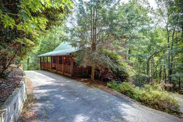 A cabin with a wooden deck and a green roof, surrounded by dense forest. - Relaxing, Cozy, Beautiful 3 BR Log Cabin in Blowing Rock/Boone NC (Blowing Rock)