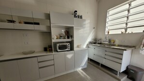 Une cuisine moderne avec des meubles blancs, un four à micro-ondes encastré et une fenêtre équipée de stores.