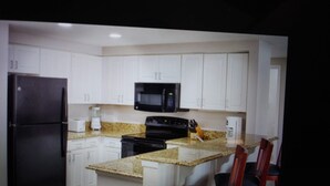 A kitchen with white cabinets, a black refrigerator, a microwave, a stove, and a granite countertop. There are two red chairs at the island.