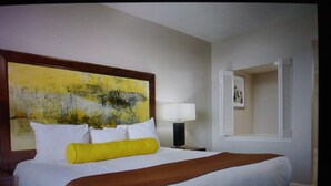 A hotel room with a large bed, a nightstand with a lamp, a painting on the wall, and a window with blinds.