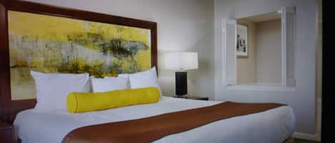 Una habitación de hotel con una cama grande, una mesita de noche con lámpara, un cuadro en la pared y una ventana con persianas.