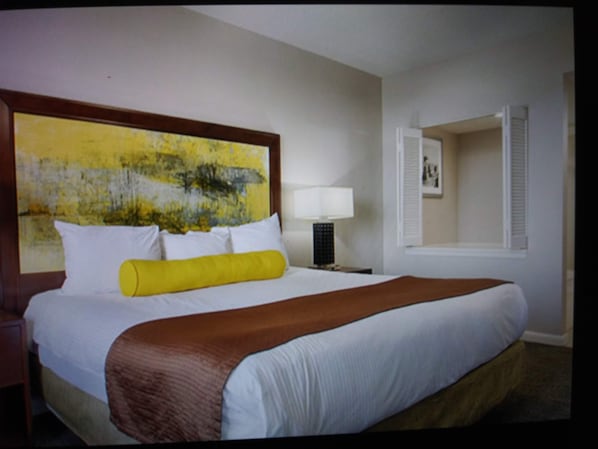 Ein Hotelzimmer mit einem großen Bett, einem Nachttisch mit Lampe, einem Bild an der Wand und einem Fenster mit Jalousien.