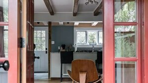 A wooden floor leading to a kitchen with a dining area, a red door, and a ceiling with exposed beams. - Modern Farmhouse on pristine private 12 Acres (Wallkill)