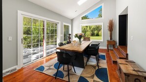 A spacious dining area with a wooden table and chairs, large windows offering a view of greenery, and a modern interior design. - Modern Farmhouse on pristine private 12 Acres (Wallkill)