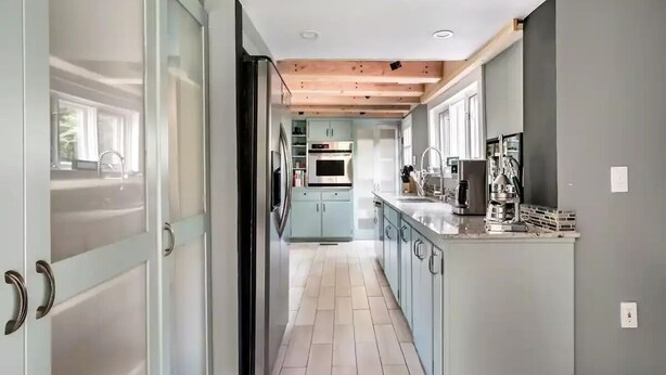 A modern kitchen with light blue cabinets, a central island, and a wooden ceiling. - Modern Farmhouse on pristine private 12 Acres (Wallkill)