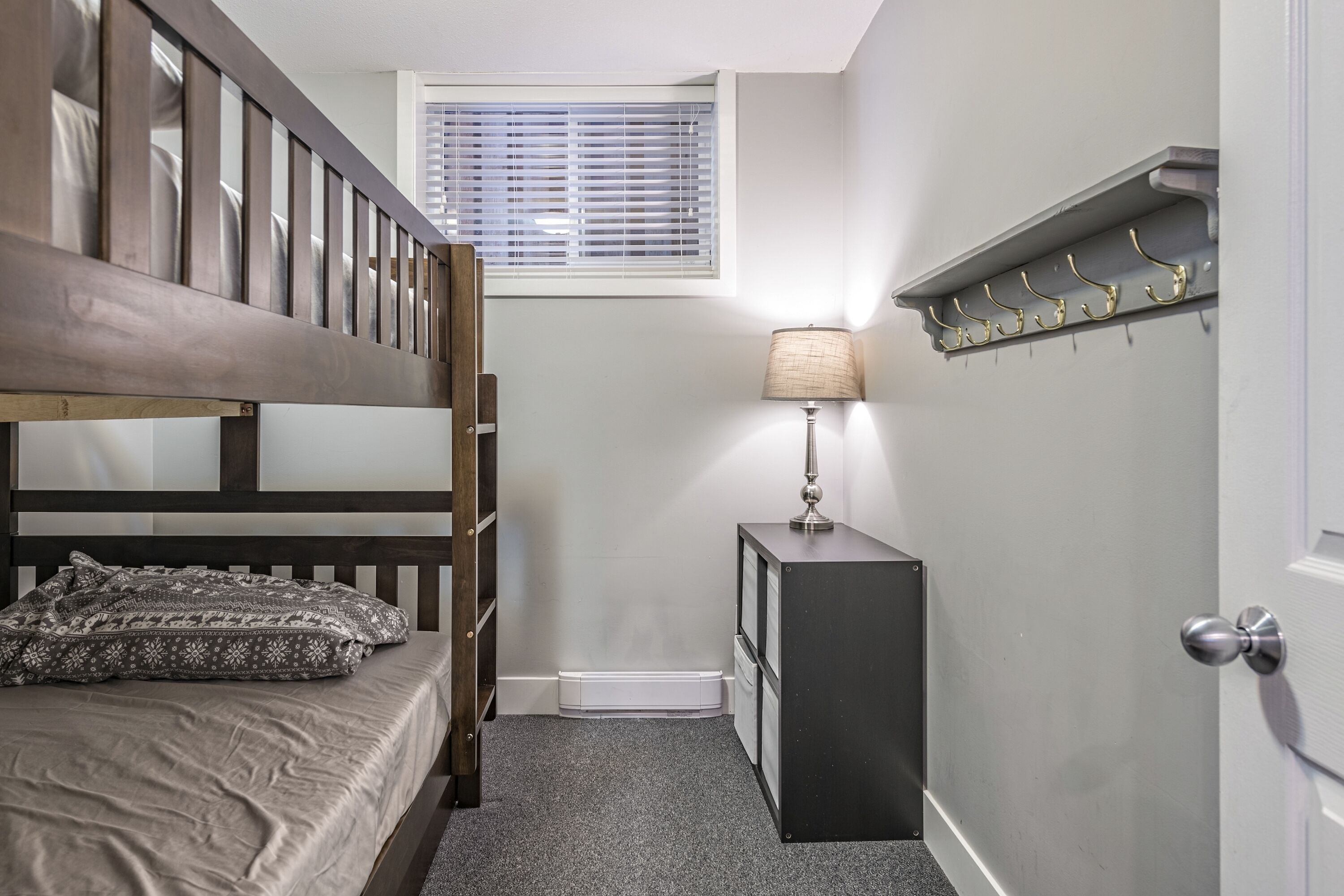 Une chambre avec un lit superposé, une table de chevet avec une lampe, un porte-manteau et une porte.
