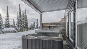 Un jacuzzi al aire libre frente a un paisaje nevado y árboles al fondo.