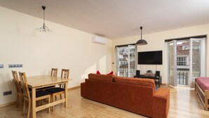 Ein Wohnzimmer mit einem Holzesstisch, Stühlen, einer Couch, einem Fernseher und einem Balkon mit Blick.