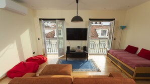 Ein Wohnzimmer mit einer Couch, einem Fernseher und einem Balkon mit Blick auf Gebäude.