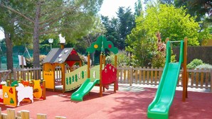 Une aire de jeux avec un toboggan, des structures d’escalade et une petite maison servant de cabane.